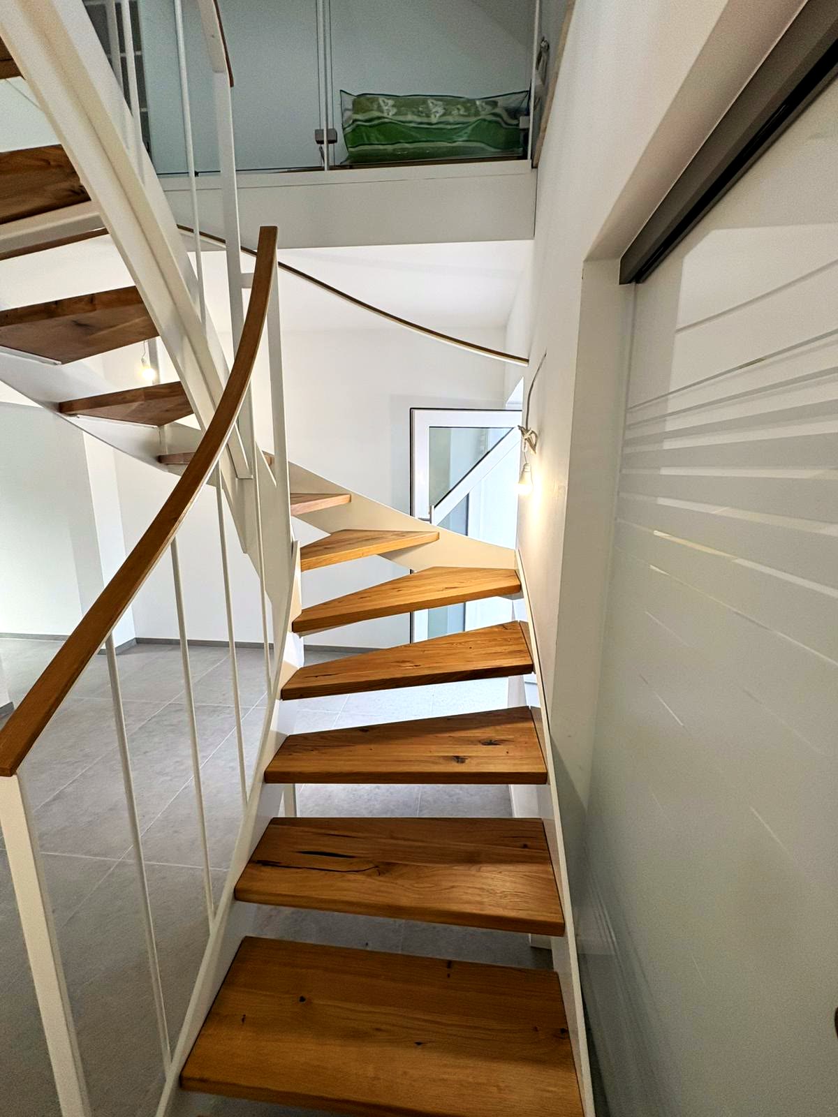 Gewendelte Treppe mit weiß beschichteter Wange, Holzstufen und Ganzglasgeländer