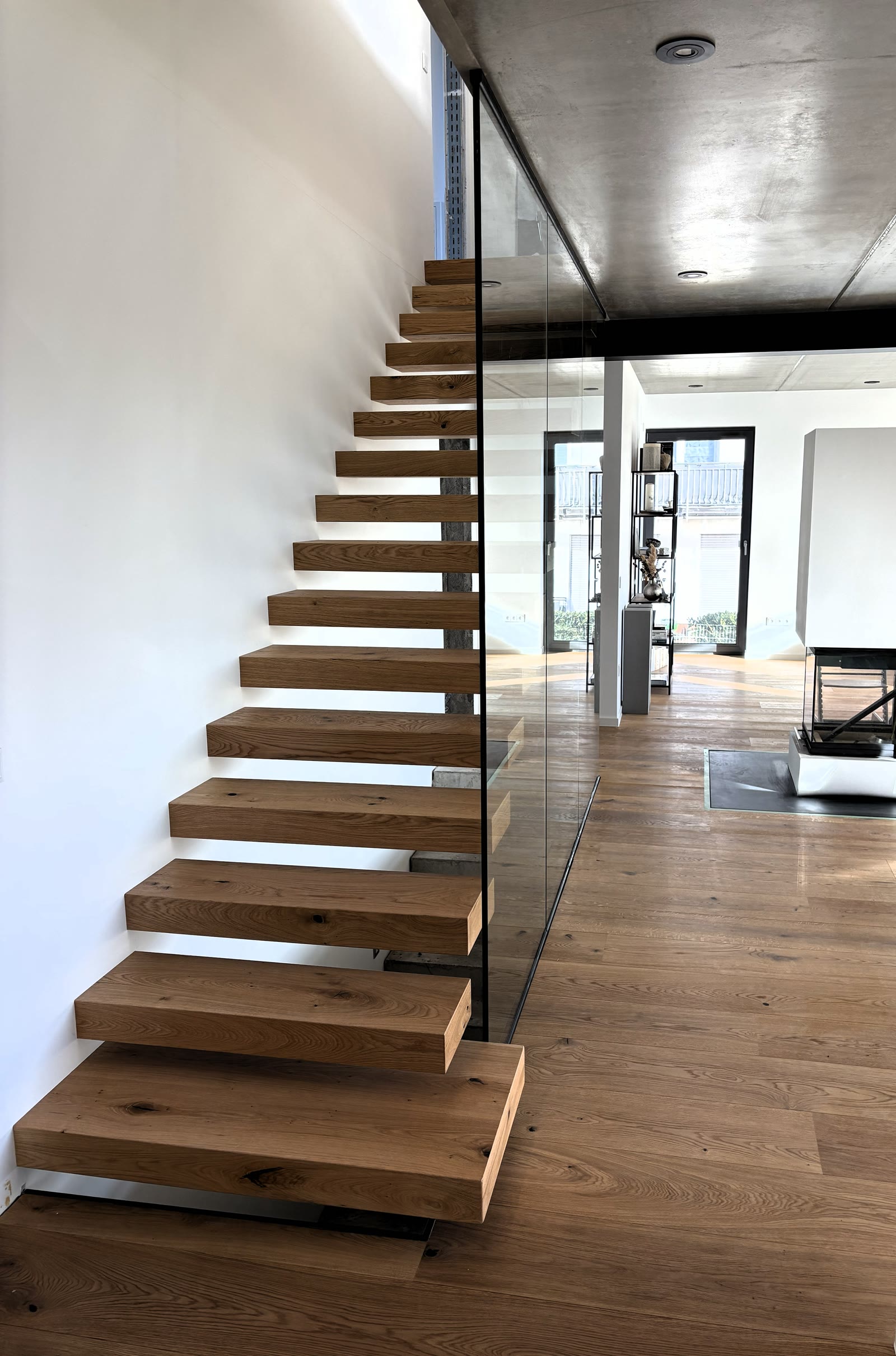 Kragarmtreppe aus Eiche mit rahmenlosem Ganzglasgeländer, Blick aus dem Wohnraum